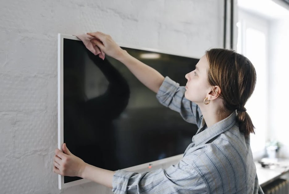 Professional cleaner carefully dusting a television.
